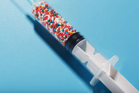 A syringe with colored balls on a blue background, free space. Top view. Concept vaccineの写真素材