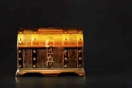 Gold treasure chest on a black textured background. Closed box with money and jewelry. Free spaceの写真素材