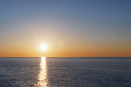 The setting sun goes into the sea on the horizon with a light track and reflections on the sea. Free spaceの写真素材