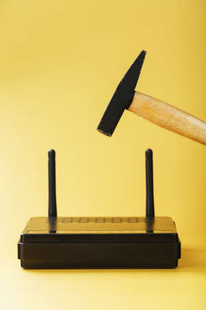 A hammer hits   modem router to break it against a yellow background. Life without internet conceptの写真素材