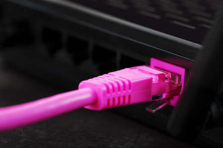A pink patch cord is inserted into the router's  port to access the Internet. Internet connection over a wire with a router. Macro, close-upの写真素材