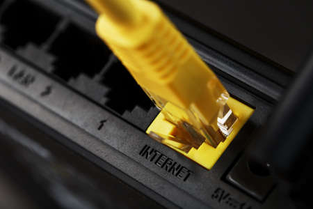 A yellow patch cord is inserted into the port of the router to access the Internet. Internet connection via a wire with a router. Macro, close-upの写真素材