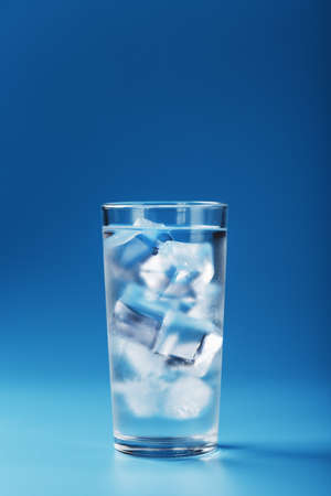 A glass with ice water and ice cubes on a blue background. A refreshing and chilling drink in hot weather. Isolate the free space.の写真素材