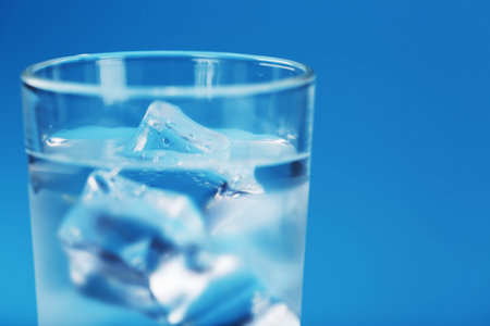 A glass with ice water and ice cubes on a blue background. A refreshing and chilling drink in hot...