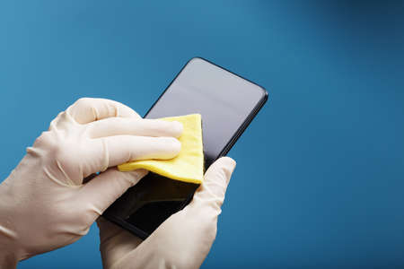 Cleaning the mobile phone screen with a yellow cloth and rubber gloves. Dirty smartphone display with germs. Soft focus. Cleaning conceptの写真素材