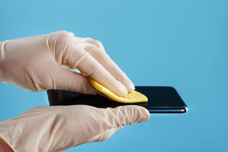 Disinfection of the smartphone with a yellow napkin with antibacterial impregnation in hand gloves. Removing coronavirus through preventionの写真素材