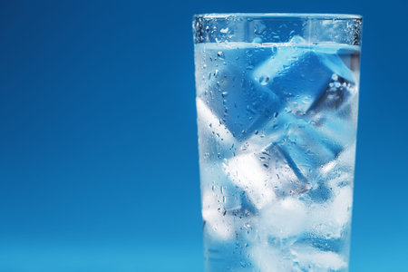 A glass with ice water and ice cubes on a blue background. A refreshing and chilling drink in hot...