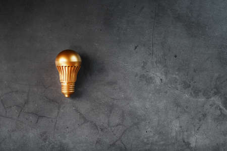 Gold light bulb on a black textured background. The concept of the idea. Free space, top viewの写真素材