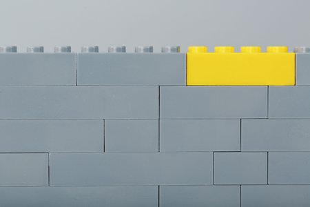 A gray wall made of a toy construction set with the last yellow brick. Concept