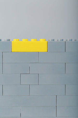 A gray wall made of a toy construction set with the last yellow brick. Concept