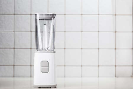 Empty electric blender in the kitchen for cocktails and healthy food. White blender on the table with light kitchen tiles. Minimal concept, copy space.の写真素材