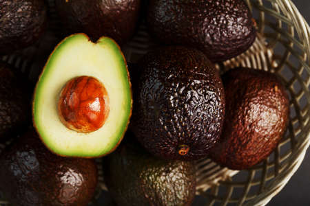 Ripe Hass avocado and a pitted slice in a basket on a black textured background. Top view, free spaceの写真素材