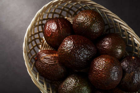 Ripe avocados in a basket on a black table, with a cut fruit and a stone. Free space, top viewの写真素材