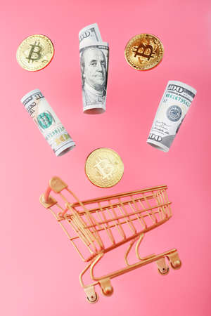 Gold mini cart with bitcoin coins and US dollars in a flight of levitation on a pink background. A shopping concept for cryptocurrency businesses, finance, trading, or stock exchange investmentsの写真素材