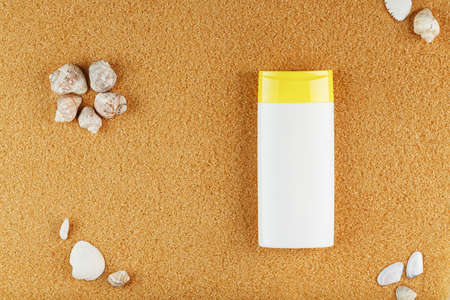 Sunscreen in a white bottle on the golden sand with shells. Free space and space for text, top viewの写真素材