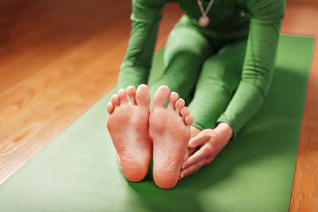 A woman does Yoga on a green rug at home in the living room. Asanas in Hatha yoga, fitness and sports at home.の写真素材