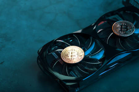 Gold bitcoin coins lie on the cooler of a powerful video card with cyanide neon illumination.の写真素材