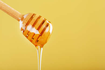 Honey drips in a thin stream from a honey dipper on a yellow background. Healthy food diet concept, ecologically pure productの写真素材