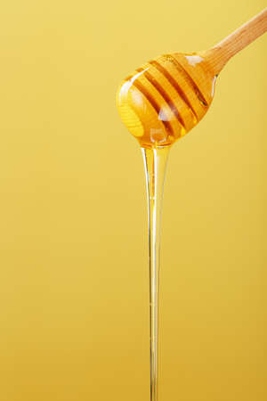 Golden honey trickles from a wooden honey dipper on a yellow background. Healthy food diet concept, ecologically pure productの写真素材