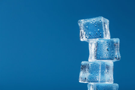 Ice cubes with water drops tower in a row on a blue background. Free space
