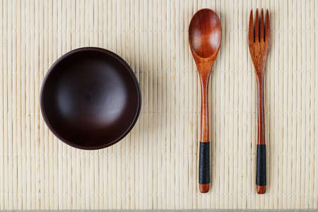Empty dark wooden cup, spoon and fork made of natural wood on a light bamboo backing. View from aboveの写真素材