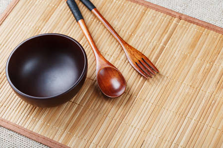 Natural wood plate, spoon and fork on a bamboo backing. Asian food handicraft concept. View from aboveの写真素材