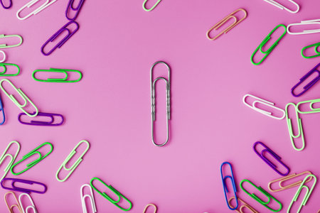 A large paper clip surrounded by small colored paper clips on a pink background.