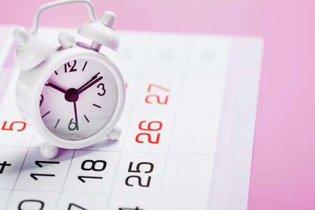 White alarm clock and calendar on a pink desktop background. Women's Days