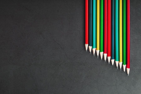 Multi-colored pencils for drawing and drawing in a row on a textured black background in a row. Top...