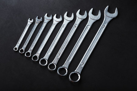 A set of wrenches on a textured black background in a row. Top view, free space