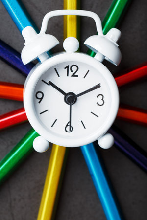 White alarm clock on Pencils of different colors in the shape of a star on a black background. The...