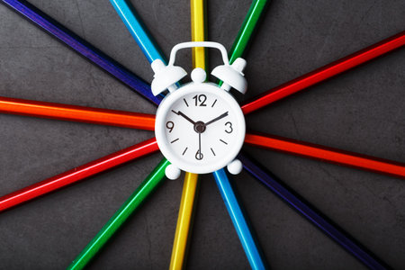 A white alarm clock with colored pencils in the shape of a star. Top view