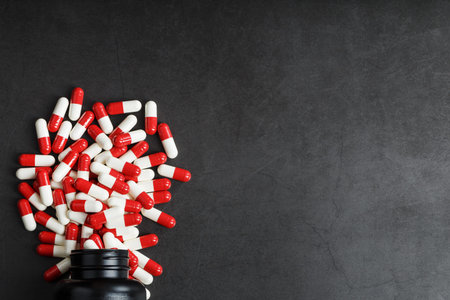 Pills with drugs are scattered from a black jar on a black background. That is a dosed solid dosage...