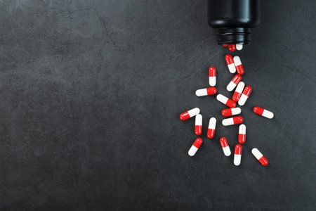 Pills with drugs are scattered from a black jar on a black background. That is a dosed solid dosage...