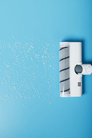 A white vacuum cleaner cleans the blue background from debris from white balls. Top view, free space