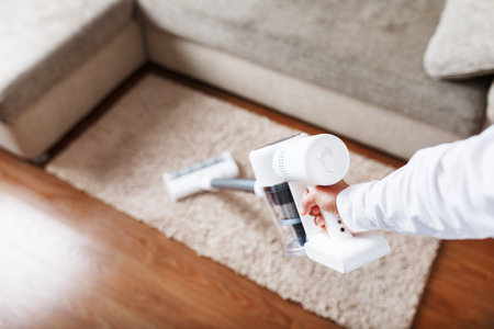 A man's hand holds a modern wireless vacuum cleaner for cleaning the sofa in the house.