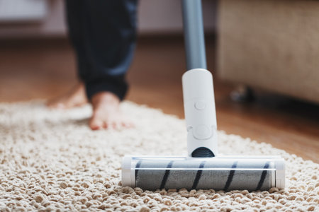Human legs and a white turbo brush of a cordless vacuum cleaner cleans the carpet in the house....