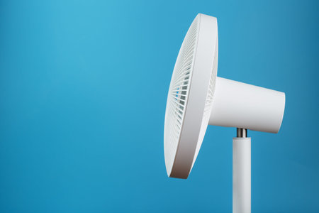 White modern electric fan for cooling the room on a blue background.