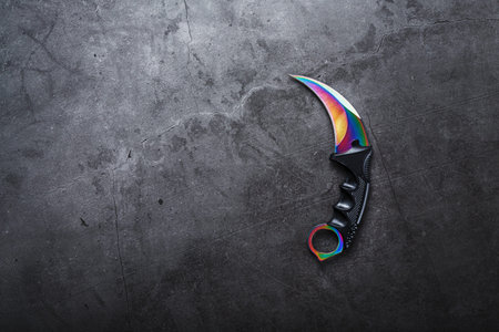 Kerambit dagger with a rainbow-colored blade on a dark textured background. Cold weapons, free space