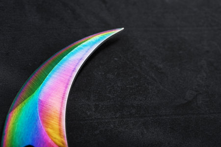 The curved sharp blade of the Kerambit Dagger is a gradient rainbow color on a dark background. Cold...