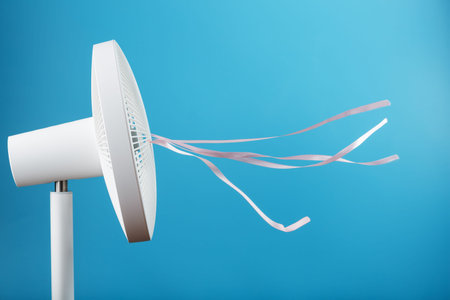 The electric fan is white with pink ribbons fluttering in the wind on a blue background. Free space,...