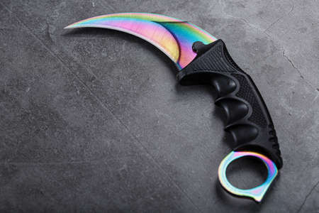 Kerambit dagger with a rainbow-colored blade on a dark textured background. Cold weapons, free spaceの写真素材