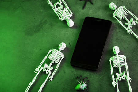 Four skeletons are lying near the smartphone on a dark background. Halloween decoration, Top view, Free spaceの写真素材