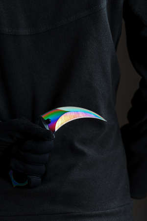A criminal with a sharp knife hidden behind his back. Curved sharp blade of rainbow-colored kerambitの写真素材