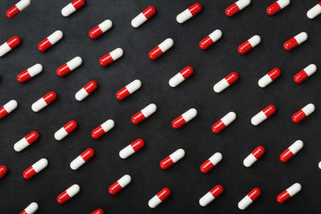 A pattern of red and white pills of medical pills on a black background. Top view, as a full-screen texture background.の写真素材