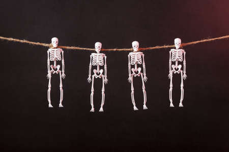 Skeletons hang on a rope on a black background with red illumination. Happy Halloween holiday.の写真素材