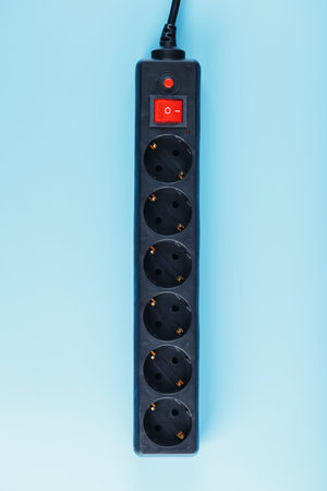 A black surge protector with portable sockets and a red button on a blue background. Free space
