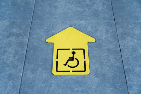 A drawing of a wheelchair on a yellow arrow glued to the tile in the waiting room. Sign Direction of movementの写真素材