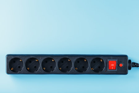A black surge protector with portable sockets and a red button on a blue background. Free space