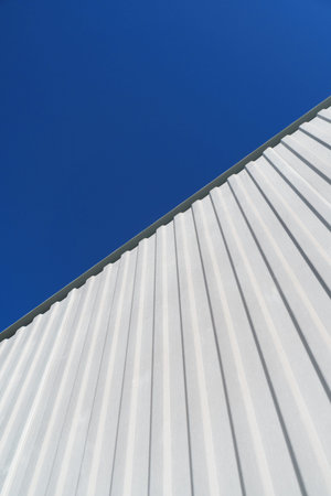 Textured white metal structures diagonally against a blue sky. Abstraction in buildingsの写真素材